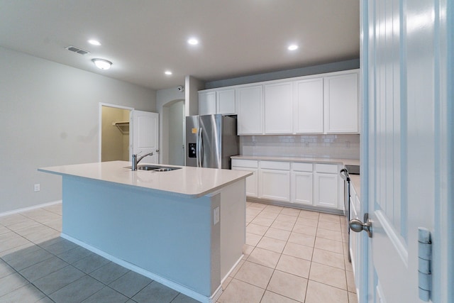 kitchen with stainless steel fridge, a center island with sink, white cabinets, and light countertops