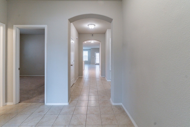 corridor with arched walkways, baseboards, and light tile patterned floors