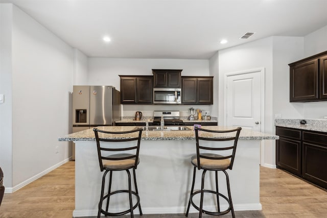 kitchen featuring visible vents, an island with sink, stainless steel appliances, dark brown cabinets, and a sink