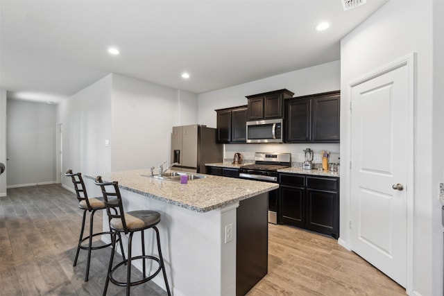 kitchen featuring stainless steel appliances, light wood-style flooring, an island with sink, and a kitchen bar