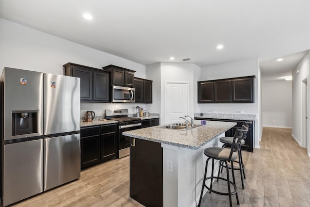 kitchen featuring light stone counters, stainless steel appliances, light wood-style floors, a kitchen island with sink, and a sink