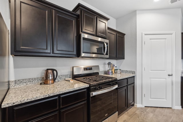 kitchen featuring light stone counters, light wood-style flooring, visible vents, dark brown cabinets, and appliances with stainless steel finishes