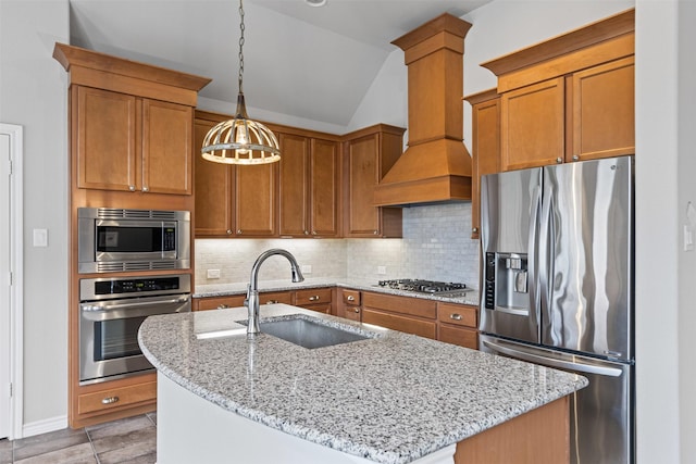 kitchen with decorative light fixtures, stainless steel appliances, a kitchen island with sink, a sink, and premium range hood