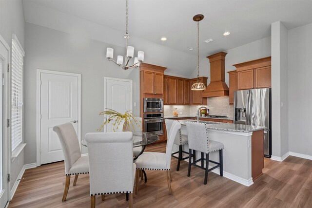 813 Louisville Rd, Aubrey, TX 76227 - kitchen featuring appliances with stainless steel finishes, custom exhaust hood, a chandelier, brown cabinetry, and vaulted ceiling