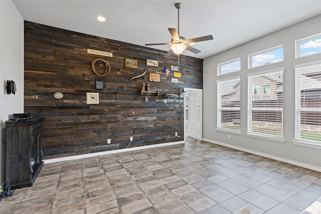unfurnished dining area with baseboards, wood walls, an accent wall, and ceiling fan