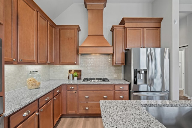 813 Louisville Rd, Aubrey, TX 76227 - kitchen featuring appliances with stainless steel finishes, premium range hood, brown cabinetry, light wood-style flooring, and backsplash