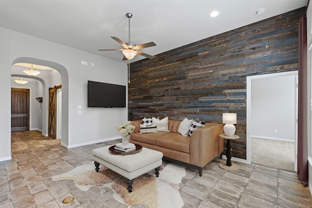 living area featuring wooden walls, baseboards, arched walkways, and ceiling fan