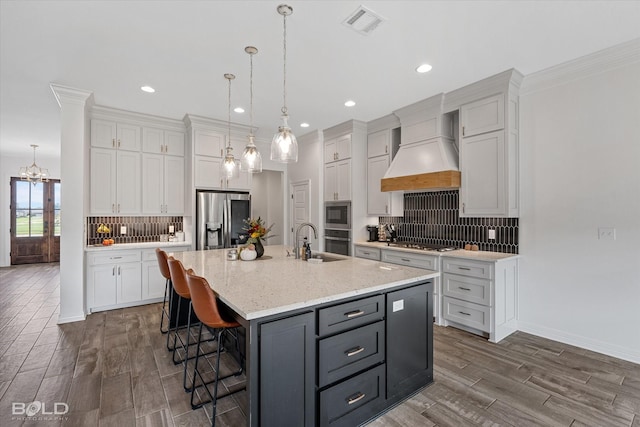 kitchen featuring an island with sink, white cabinetry, custom exhaust hood, and stainless steel appliances