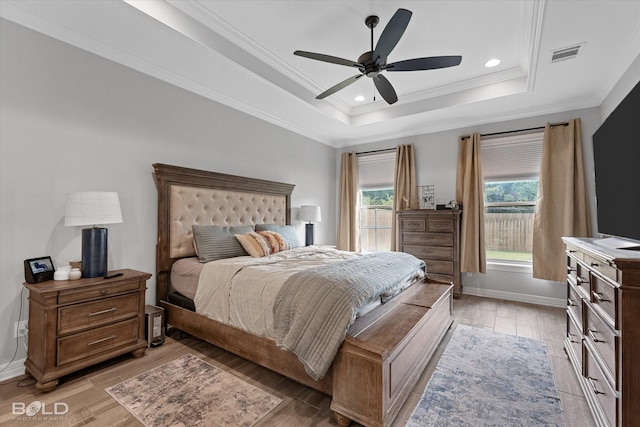 bedroom with light wood finished floors, visible vents, and a tray ceiling