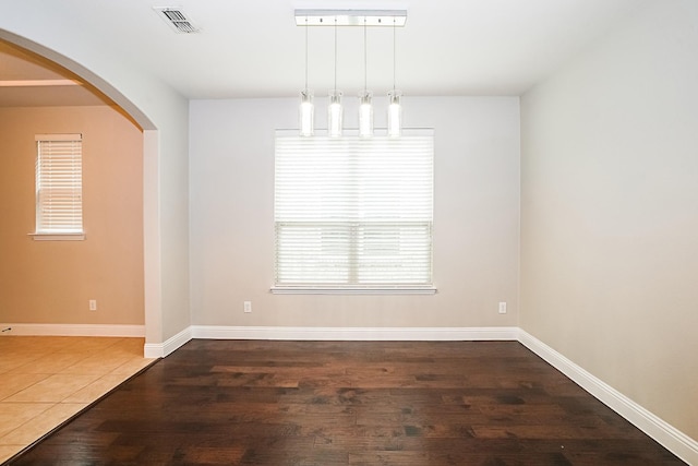 unfurnished dining area featuring arched walkways, dark wood-style floors, visible vents, and baseboards