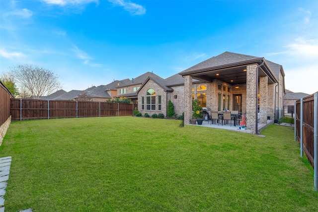 rear view of property with brick siding, a fenced backyard, a lawn, and a patio