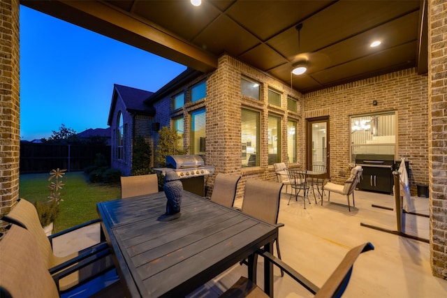 patio terrace at dusk with outdoor dining space, a grill, ceiling fan, and fence