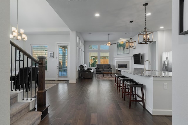 kitchen with open floor plan, stainless steel refrigerator with ice dispenser, light stone countertops, a tiled fireplace, and decorative light fixtures