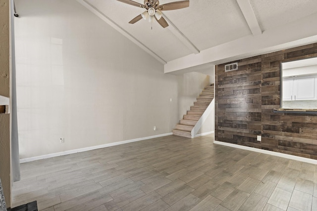 unfurnished living room featuring vaulted ceiling with beams, ceiling fan, wood finished floors, baseboards, and stairway