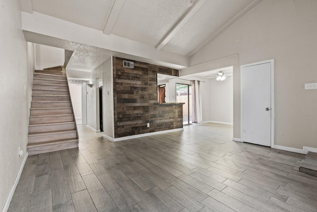 unfurnished living room featuring visible vents, lofted ceiling with beams, stairway, wood tiled floor, and a textured ceiling