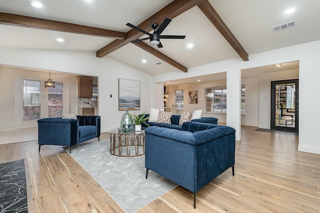 living room featuring light wood-type flooring, vaulted ceiling with beams, plenty of natural light, and visible vents