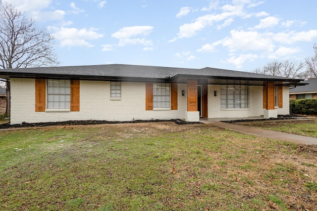 view of front of home with a shingled roof, a front yard, and brick siding