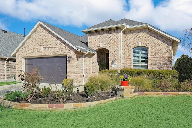 french country style house featuring brick siding, an attached garage, a shingled roof, and a front yard