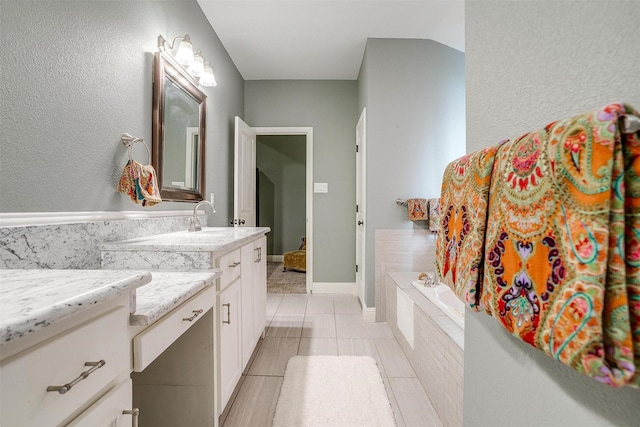 bathroom featuring lofted ceiling, a garden tub, vanity, and baseboards