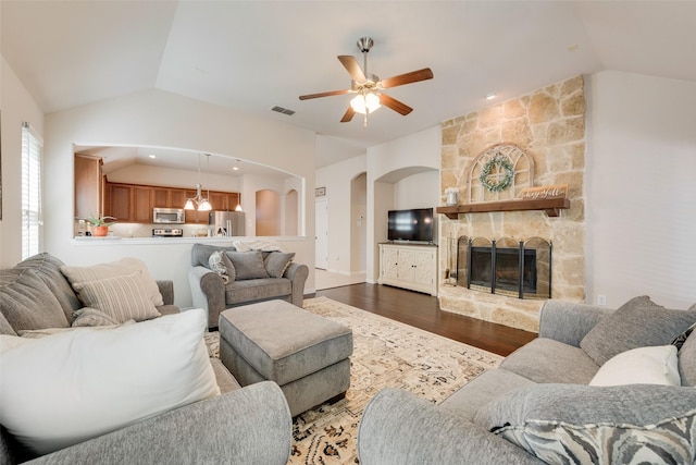 living room featuring lofted ceiling, visible vents, dark wood-style flooring, and a stone fireplace