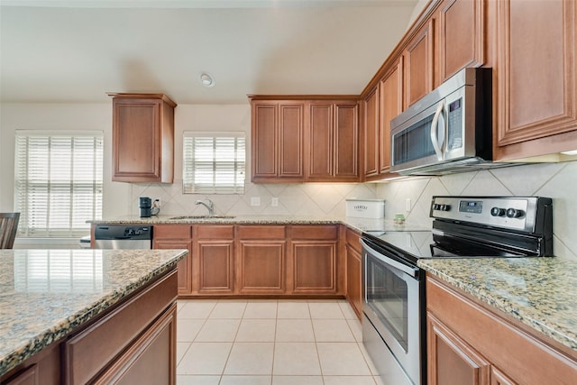 kitchen featuring light stone counters, brown cabinets, appliances with stainless steel finishes, light tile patterned flooring, and a sink