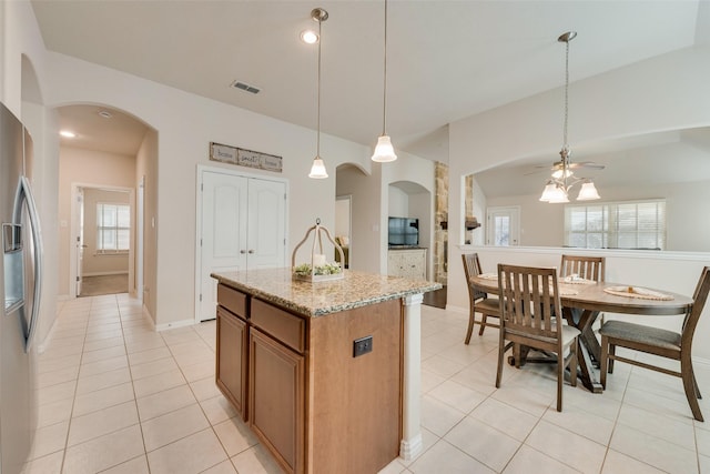 kitchen featuring light stone counters, pendant lighting, open floor plan, an island with sink, and stainless steel fridge