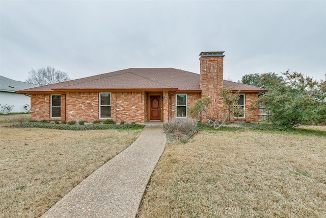 single story home with a shingled roof, a front yard, a chimney, and brick siding