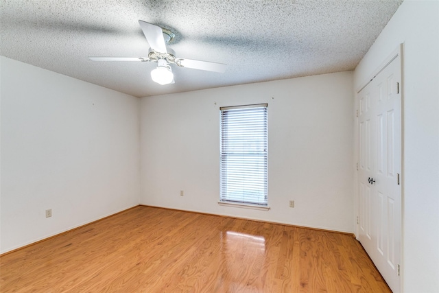 empty room with a ceiling fan, light wood-style flooring, and a textured ceiling