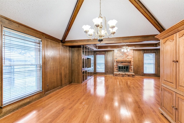 unfurnished living room with vaulted ceiling with beams, light wood finished floors, a brick fireplace, wood walls, and a textured ceiling