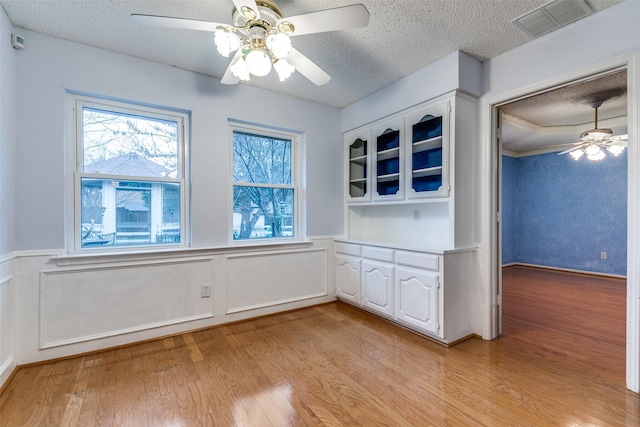 interior space featuring wainscoting, visible vents, a textured ceiling, and light wood finished floors