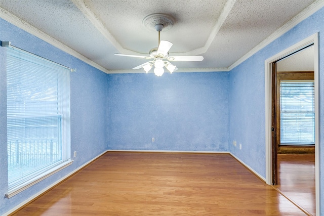 empty room featuring light wood-style floors, a raised ceiling, ornamental molding, and a ceiling fan