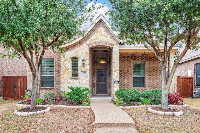 view of front of home featuring stone siding, brick siding, and fence