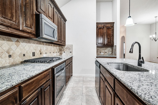 kitchen featuring decorative light fixtures, stainless steel appliances, a sink, dark brown cabinets, and light stone countertops