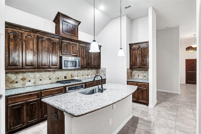 kitchen featuring dark brown cabinetry, appliances with stainless steel finishes, decorative light fixtures, light stone countertops, and a sink