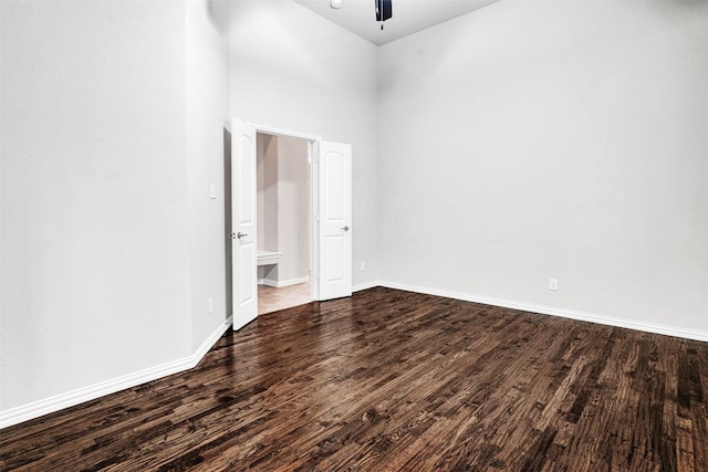 empty room with dark wood-style floors, ceiling fan, a high ceiling, and baseboards