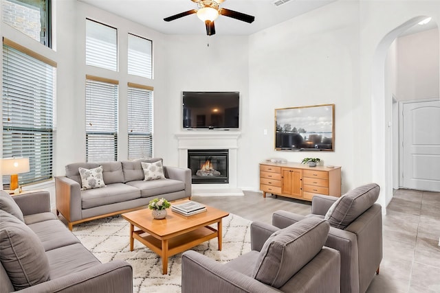 living room with visible vents, arched walkways, a glass covered fireplace, ceiling fan, and a high ceiling