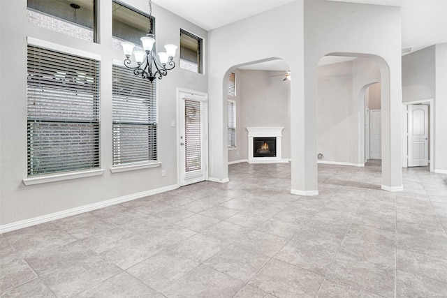 interior space featuring arched walkways, a high ceiling, visible vents, baseboards, and a glass covered fireplace