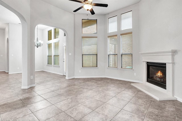 unfurnished living room featuring arched walkways, light tile patterned floors, ceiling fan with notable chandelier, and baseboards