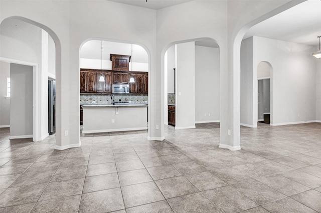 unfurnished living room featuring a towering ceiling, light tile patterned floors, and baseboards