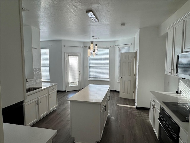 kitchen with decorative light fixtures, a center island, light countertops, black appliances, and white cabinetry