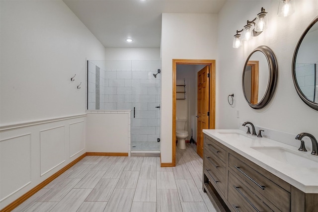 bathroom featuring toilet, a stall shower, a decorative wall, and a sink