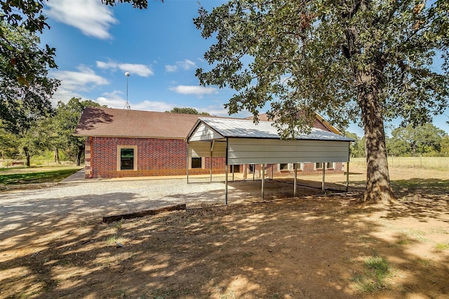 rear view of property featuring dirt driveway, brick siding, and a detached carport