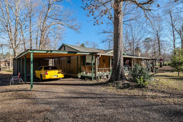 view of front facade featuring covered porch, dirt driveway, a chimney, and an attached carport