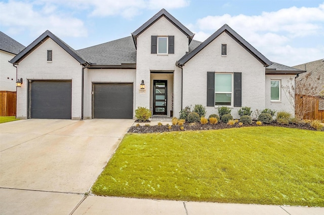 french country home with brick siding, concrete driveway, an attached garage, fence, and a front lawn