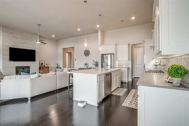 kitchen with an island with sink, appliances with stainless steel finishes, open floor plan, decorative light fixtures, and light countertops