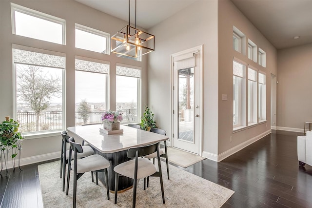 dining room featuring a towering ceiling, an inviting chandelier, baseboards, and dark wood finished floors