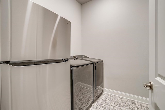 clothes washing area with laundry area, washing machine and dryer, light tile patterned floors, and baseboards