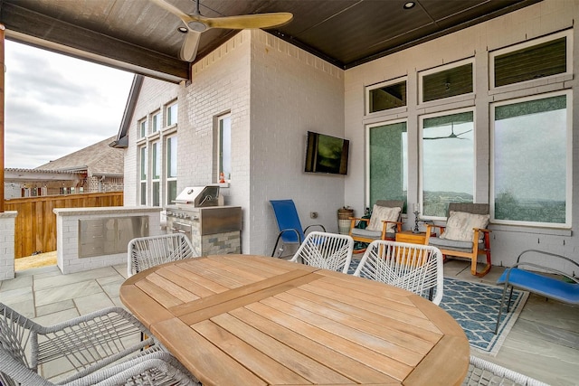 view of patio with ceiling fan, outdoor dining area, fence, exterior kitchen, and grilling area