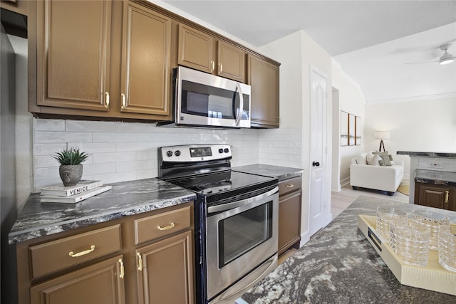 kitchen with stainless steel appliances, a ceiling fan, open floor plan, backsplash, and dark stone counters