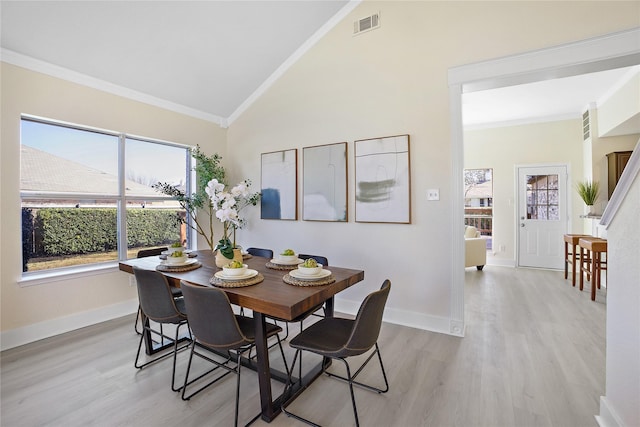 dining room featuring vaulted ceiling, light wood-style floors, visible vents, and crown molding